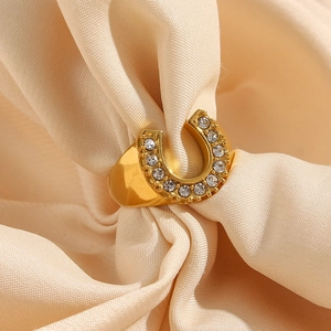 Macro detail of 18K gold plated U-shape ring with clear zircons on beige satin fabric