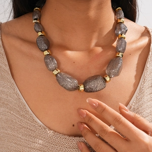 Macro detail of large grey glitter beads with gold link chains on a textured sweater