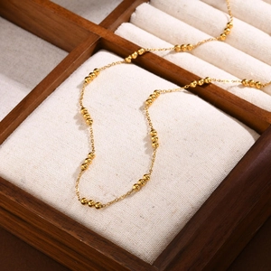 Macro shot of gold stainless steel necklace with beads on textured linen tray
