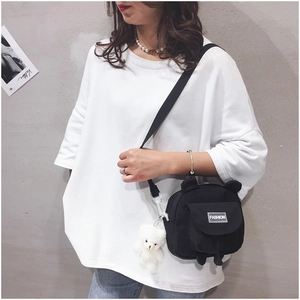 Detail of black bear-ear canvas crossbody bag featuring a white bear plush keychain