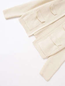 Dettaglio ravvicinato della trama in maglia e della tasca di un cardigan oversize crema
