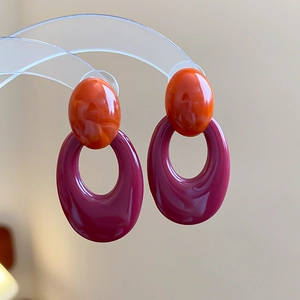 Detail view of retro acrylic earrings with orange and purple hollow oval pendants on a stand