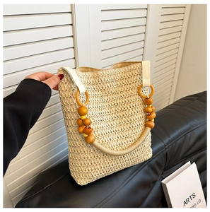 Detail of beige straw tote bag featuring decorative yellow and brown wooden bead handles