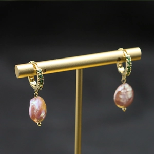 Detail of baroque pearl earring with green emerald stones on a golden metal hoop
