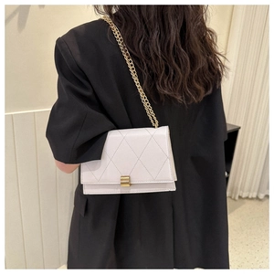 Detailed view of cream quilted shoulder bag with gold chain strap on a black blazer