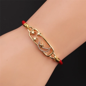 Detail of gold star and moon charms with zircon on a red braided rope bracelet