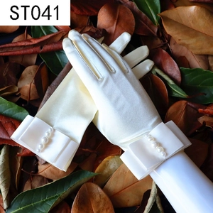Detail of white satin bridal gloves featuring pearl bow design on dry leaf background