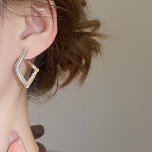 Close-up of model wearing geometric diamond-shaped silver hoop earring in polished finish