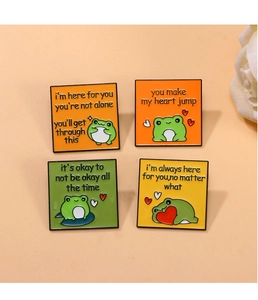 Detail of four square enamel pins featuring green frog characters and supportive quotes