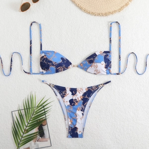 Flat lay of baroque print bikini with gold scrolls and vacation accessories on sand