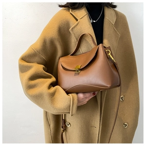 Close-up of a brown vintage leather handbag with a gold lock on a camel coat background