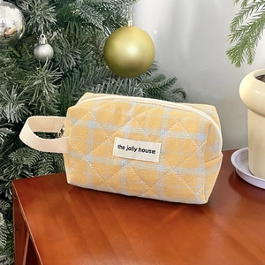 Close-up of yellow checkered quilted cosmetic bag with woven handle and brand label