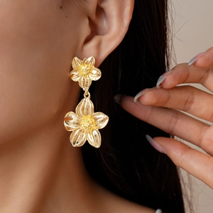 Detail shot of a model wearing double-layered gold flower earrings with natural textures