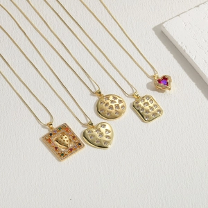 Cinq colliers dorés avec pendentifs géométriques en zircon en formes de cœur et de carré sur blanc