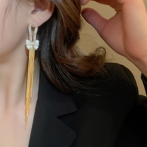 Close-up of elegant gold bow earrings with long tassels and zircons worn by a model