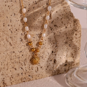 Detail of freshwater pearl necklace with golden sun pendant on beige natural stone