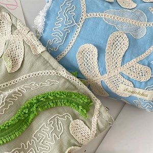 Close-up of 3D flower embroidery and lace details on sage green and blue makeup bags
