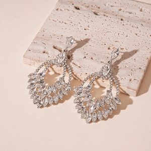 Dettaglio di orecchini a goccia argento con strass marquise su pietra beige