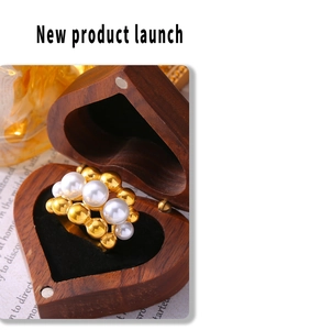Macro shot of gold bead and pearl ring presented in a heart-shaped wooden jewelry box