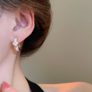 Détail d'une boucle d'oreille en émail blanc en forme de C avec cœur doré sur mannequin
