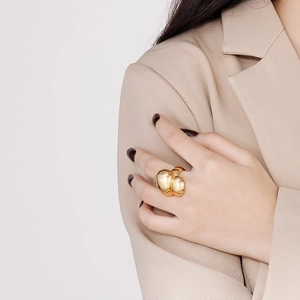 Close-up of a chunky golden sculptural ring with a polished mirror finish on a model's hand