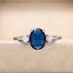 Elegante anello con gemma blu ovale e pietre laterali su castone in tonalità argento