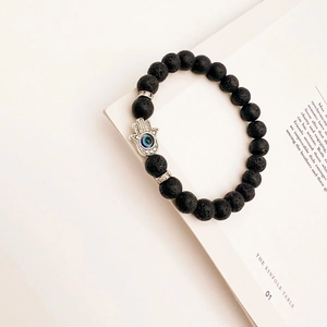 Detail of black lava stone beads and silver Hamsa Hand charm with blue evil eye on a book