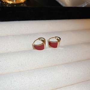 Macro shot of minimalist gold crescent earrings with red enamel on a velvet tray