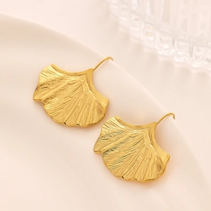 Détail de boucles d'oreilles feuille de ginkgo dorée avec nervures sur plateau crème