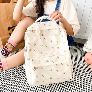 Detailed view of the floral patterned beige backpack worn by a model in a casual setting