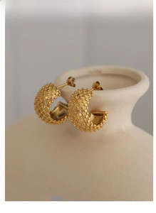 Detail of gold C-shaped earrings with beaded texture hanging on ceramic decor