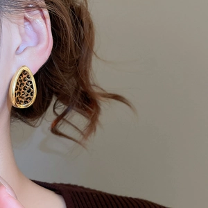 Close-up of leaf-shaped leopard print stud earrings with golden trim worn by a model