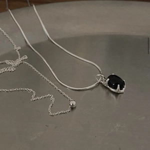 Close-up of a silver snake chain necklace featuring a polished oval black onyx pendant