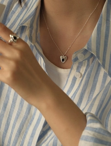 Close-up of a silver heart necklace and matching ring with black enamel drip on model