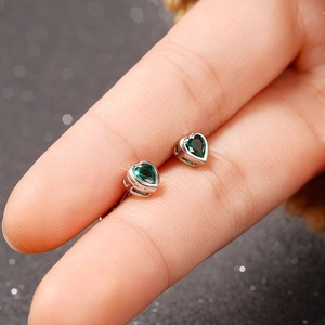 Macro detail of heart-shaped green zircon studs with polished silver metal setting
