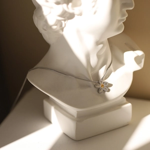Detail of silver daisy pendant with yellow core on a necklace over white bust