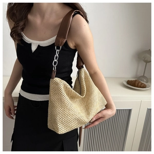 Detail of beige woven straw shoulder bag with brown leather strap and silver chain link