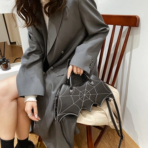 Detailed view of black bat shaped handbag with white spider web embroidery and spider charm