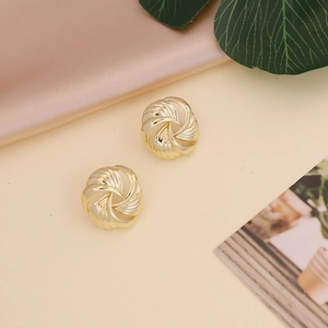 Nahaufnahme goldener runder Ohrstecker mit Spiralstruktur auf Seide und Blättern
