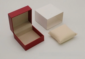 Detail view of red textured flip watch box with white outer sleeve and beige pillow
