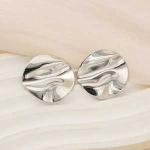 Vue macro de boucles d'oreilles argentées aux ondulations irrégulières et fini miroir