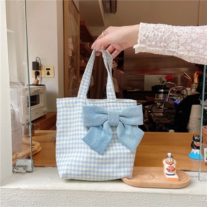 Detail of blue gingham plaid lunch bag with a large denim bow held by a hand