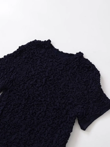 Macro detail of textured knit fabric with pleated surface on a navy crew neck top