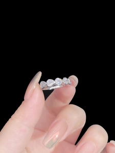 Macro detail of hand holding silver ring with five heart-cut cubic zirconia stones