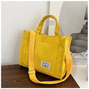 Close-up of yellow corduroy tote bag showing adjustable strap and white woven label