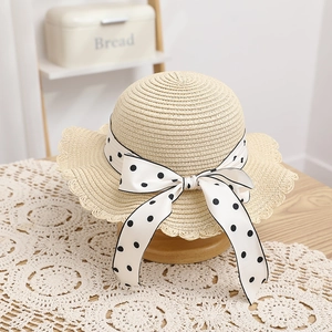 Detail of child straw hat with polka dot ribbon bow and wavy brim edge on display