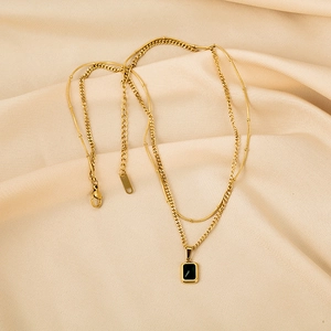 Détail d'un collier double rang doré avec zircon émeraude rectangulaire et fermoir mousqueton
