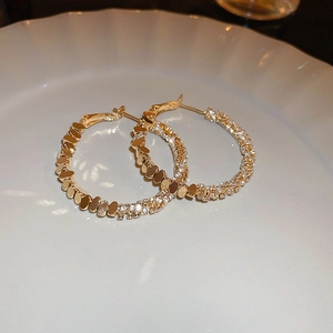 Gros plan de créoles dorées serties de zircons blancs sur une assiette en céramique