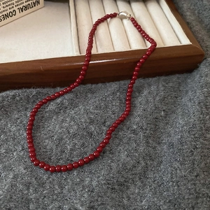 Detail of deep red glass beads necklace with silver clasp on a wooden jewelry tray