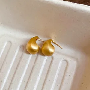 Minimalist gold teardrop stud earrings with a matte brushed finish on a neutral tray